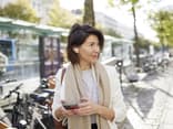 Frau mit Handy auf der Straße trägt halblange Frisur ab 50