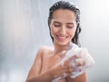 Frau seift Körper ein unter der Dusche