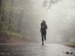 Frau beim Joggen bei Regen im Wald.