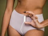 Frau hält einen Tampon vor ihrem Unterleib in der Hand.