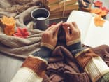 Frau strickt und hat ein Strickbuch parat