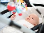 Baby liegt im Kinderwagen und schaut seine Kinderwagenkette