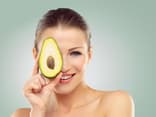 Diese Lebensmittel gelten als Fatburner: Frau hält Avocadohälfte